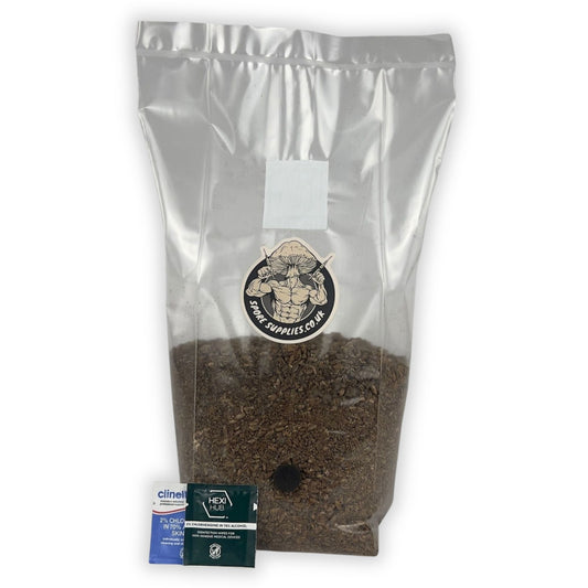A sealed, clear plastic bag filled with brown substrate, labeled as a 'Wood-Based All In One Mushroom Grow Bag'. A small blue isopropyl wipe is in front to use when inoculating the bag.