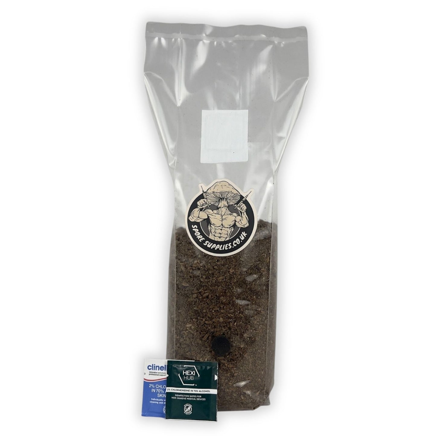 A sealed plastic bag containing a wood-based all in one mushroom grow bag, with a label showing a mushroom image and brand name, alongside a small blue isopropyl wipe.