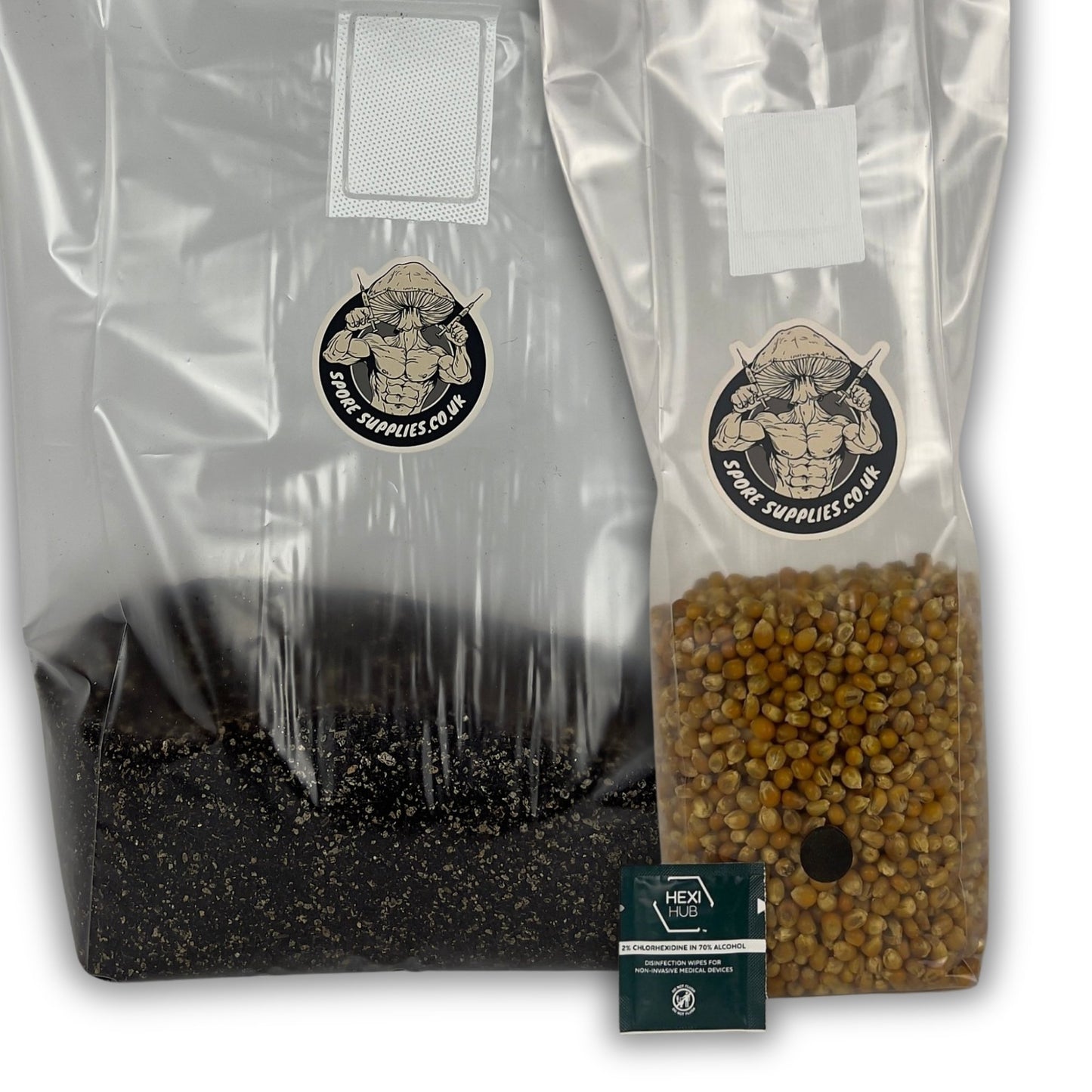 Two clear plastic grow bags on a white background, one filled with dark substrate and the other with popcorn grain, both printed with the Spore Supplies logo. A small isopropyl wipe packet is placed in front.